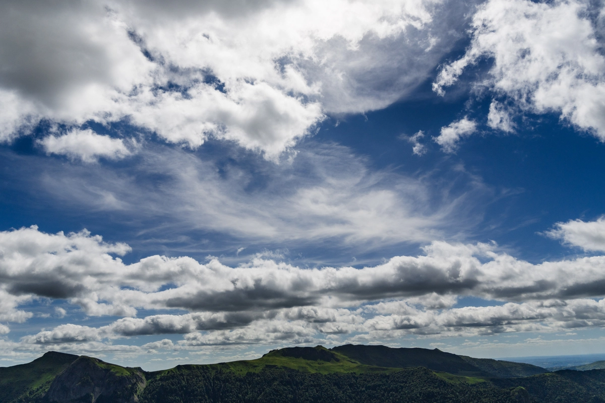 A vast dramatic sky of streaked and billowing clouds above a low, dark green mountain range on the horizon