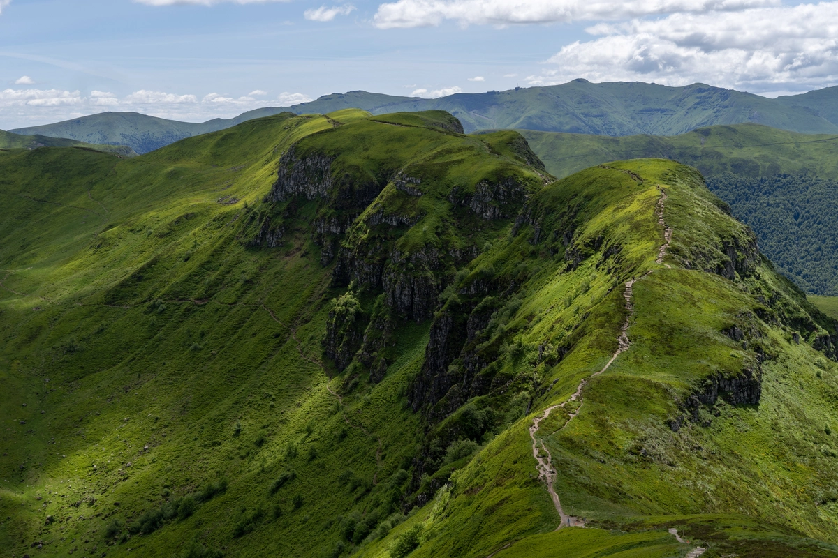 Green volcanic ridges with a footpath winding along a grassy crest above steep rocky cliffs