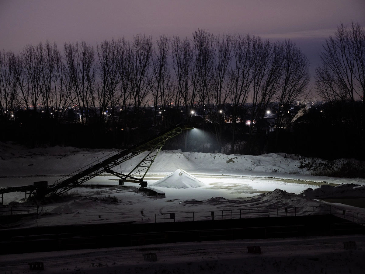 Snow-covered industrial site with conveyor belt lit up at dusk