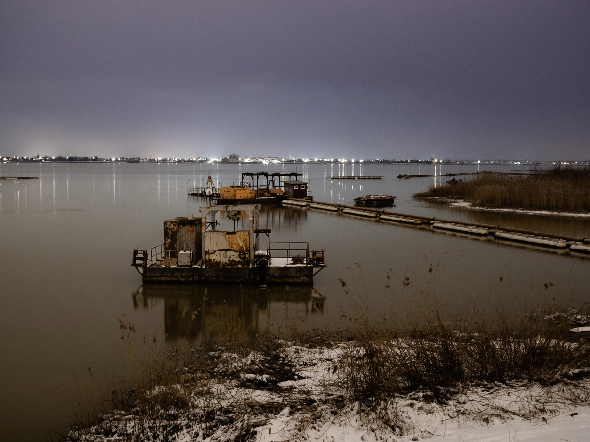 Dredging barge on a still lake at night with distant city lights