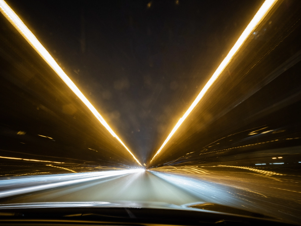Long-exposure light trails converging inside a highway tunnel at night