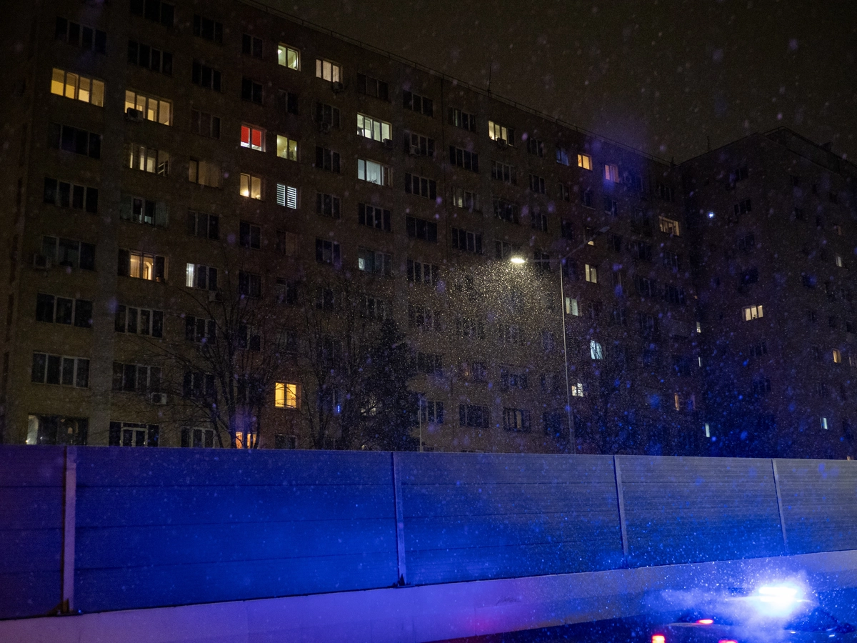 Communist-era apartment block with lit windows during a nighttime snowfall