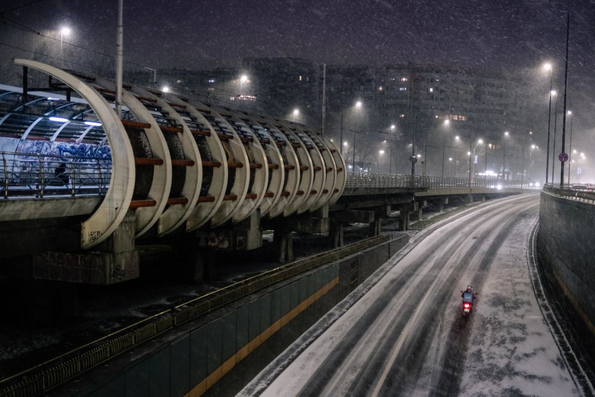 Snow-dusted highway underpass with streetlights and a lone red taillight