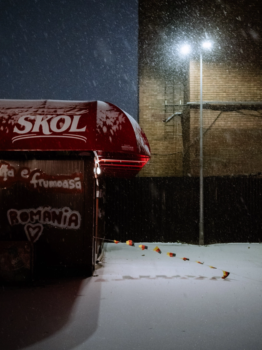 Red Skol beer kiosk with România graffiti sitting in fresh snow at night